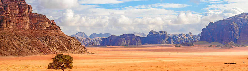 Woestijnlandschap in Wadi Rum, Jordanië, met rode zandvlakte en rotsformaties onder een bewolkte lucht.
