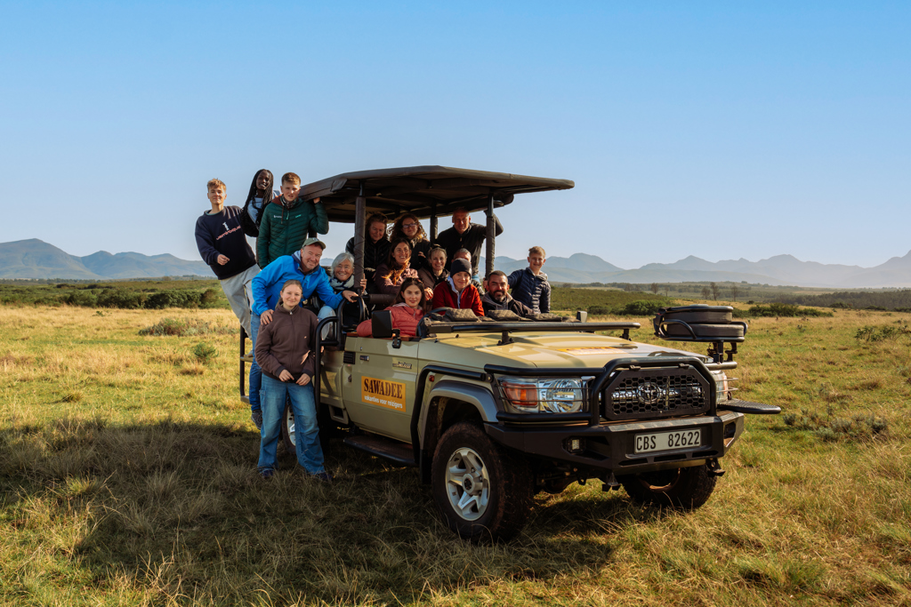 Familiereis Zuid-Afrika: groep in safarijeep tijdens game drive, met bergen op de achtergrond.