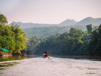 Longtailboot op de rivier bij Kanchanaburi, omringd door jungle en bergen in Thailand.