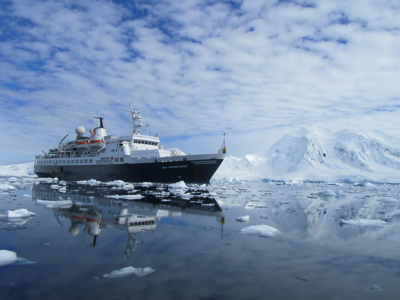 Expeditieschip vaart tussen drijvend ijs langs besneeuwde bergen op Antarctica-route.