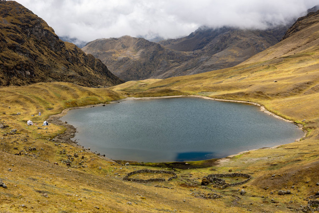 Bergmeer in de Peruaanse Andes met kampeerplek en wolken boven de bergen.