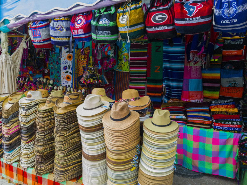 Kleurrijke markt in Mexico met stapels strohoeden en geweven dekens, een leuk uitstapje tijdens een familiereis.