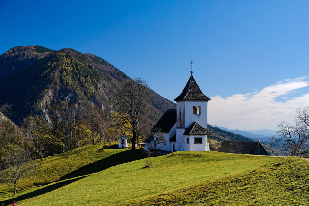 Kerkje op groene heuvels met bergen op de achtergrond in Slovenië, tijdens een groepsrondreis.