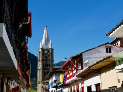 Kerk met hoge toren tussen kleurrijke huizen en Colombiaanse vlaggen, route door Colombia.