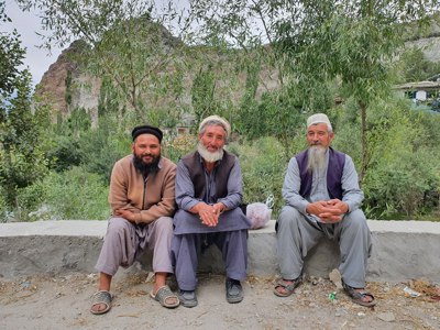 Drie mannen zitten op een muurtje in een groen bergdorp in Baltistan, Pakistan.