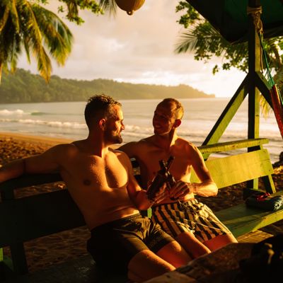 Twee vrienden ontspannen met een drankje op een bankje aan het strand in Costa Rica bij zonsondergang.