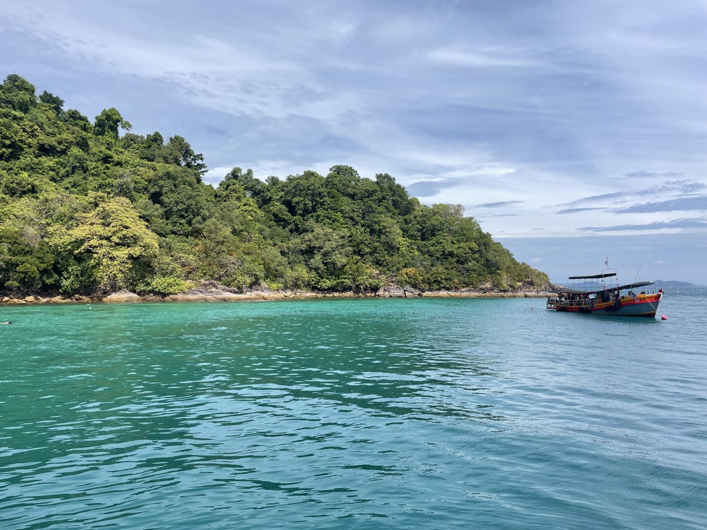 Boot op helderblauw water langs een groen eiland tijdens 22-35ers reis Thailand, Laos & Cambodja.