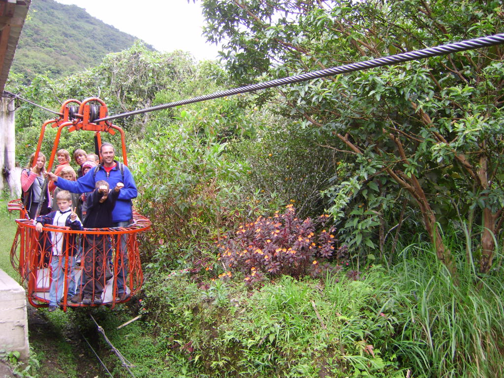 Gezin in kabelbaanmandje boven groen berglandschap tijdens familiereis Ecuador.