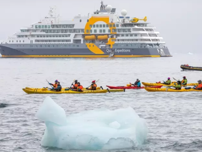Kajakkers peddelen tussen drijvend ijs met expeditieschip op de achtergrond tijdens de rondreis Antarctica.
