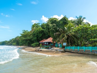 Tropisch strand in Cahuita, Costa Rica, met palmbomen en kleurrijke huisjes aan de kust.