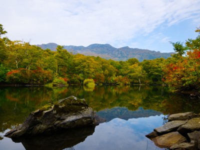 Herfstkleuren rond een rustig bergmeer in Japan, met weerspiegeling van het bos in het water.
