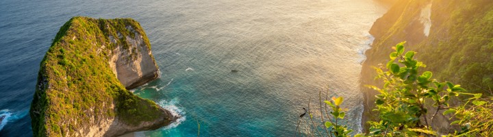 Uitzicht op Kelingking Beach op Nusa Penida met steile kliffen, turquoise zee en zandstrand bij zonsondergang.