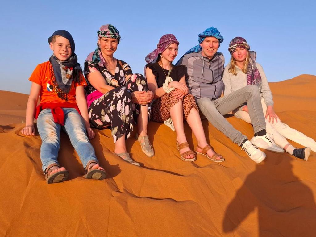Gezin met hoofddoeken zit op zandduinen in de Sahara tijdens familiereis Marokko Hoogtepunten.