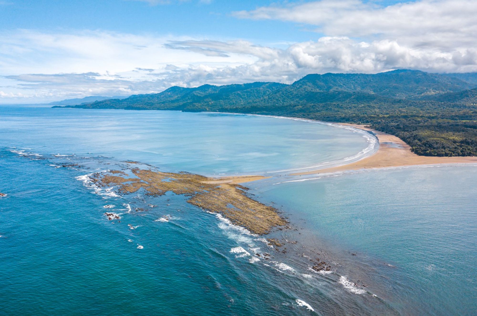een brede baai met zandstrand en groene bergen aan de kust van Costa Rica.