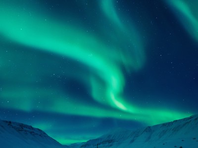 Noorderlicht boven besneeuwde bergen op Spitsbergen, met groene lichtbogen in een heldere sterrenhemel.