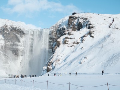 Besneeuwde Skógafoss-waterval in IJsland in de winter, met bezoekers op het uitkijkpunt.