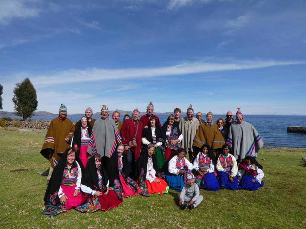 Groepsfoto tijdens groepsrondreis Peru met locals in traditionele kleding aan het Titicacameer.