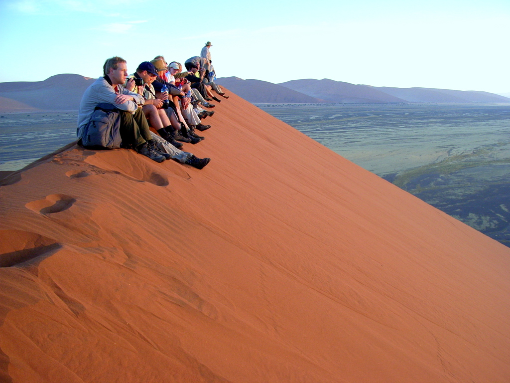 Reizigers zitten op een hoge zandduin in Namibië tijdens een groepsrondreis Zuidelijk Afrika.