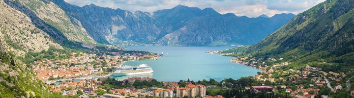 Uitzicht op de Baai van Kotor in Montenegro met bergen, kustplaatsen en een cruiseschip.