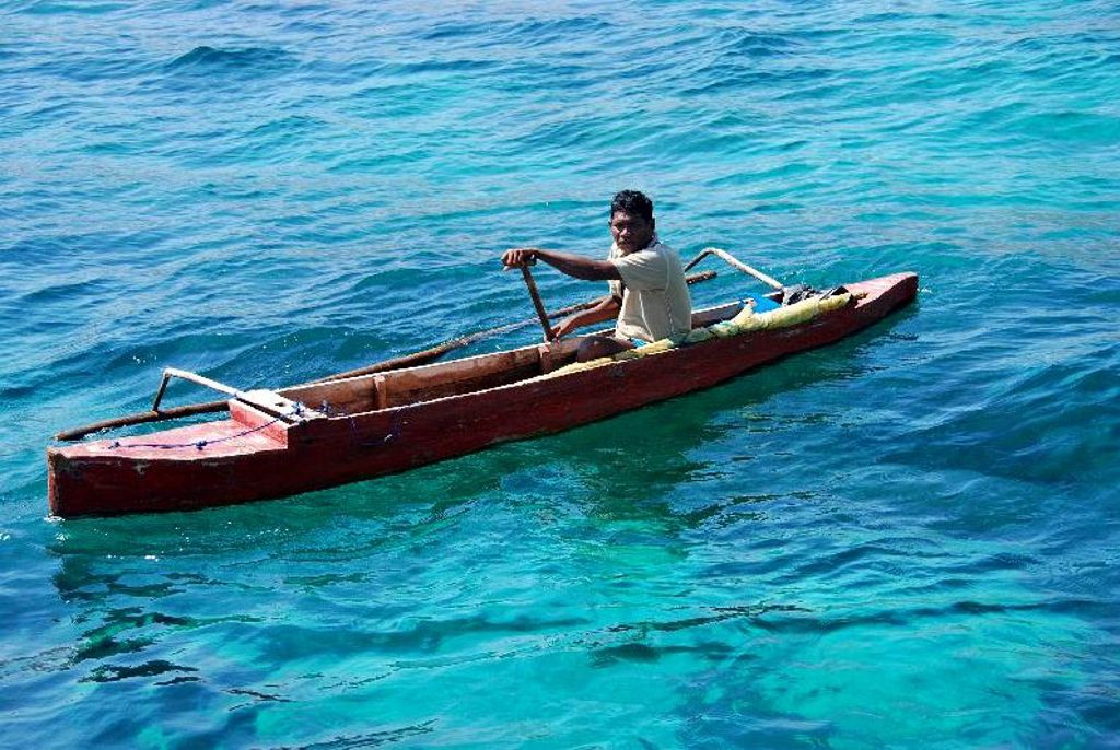 Man in houten kano op helderblauw zeewater bij de Kleine Sunda eilanden, Indonesië.