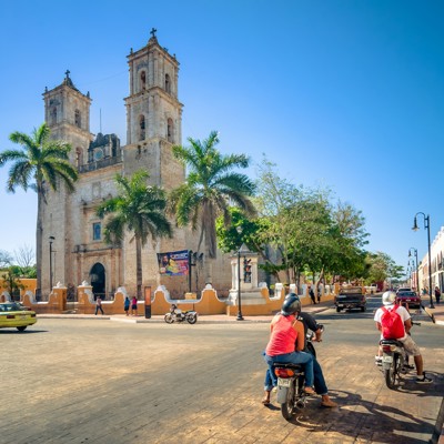 Straatbeeld in Mexico met koloniale kerk, palmbomen en scooters, onderdeel van Familiereis Mexico hoogtepunten.