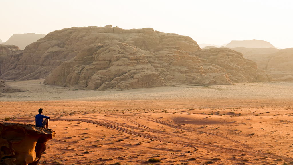 Reiziger kijkt uit over de Wadi Rum-woestijn met zandvlaktes en rotsformaties tijdens een 22-35ers reis Jordanië.