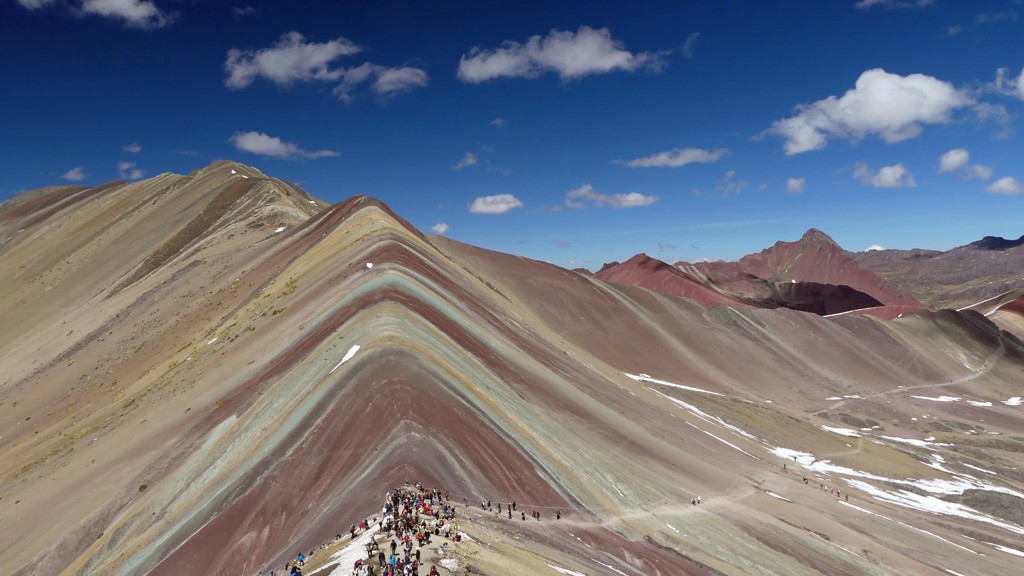Gekleurde Rainbow Mountain (Vinicunca) in Peru met wandelaars op de bergkam onder een blauwe lucht.