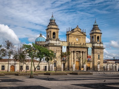 Kathedraal van Guatemala-Stad aan het centrale plein, met twee klokkentorens en blauwe koepel onder een heldere lucht.