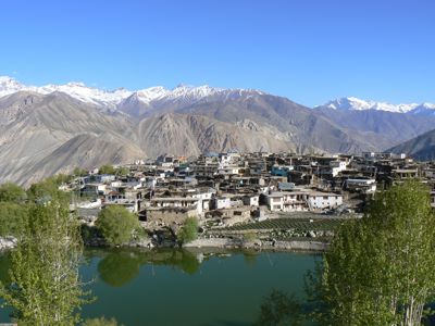 Dorp aan een rivier met terrassen, met besneeuwde Himalayatoppen op de achtergrond in Spiti & Ladakh-route.