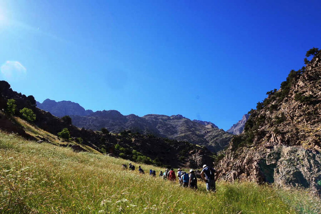 Wandelaars tijdens de beklimming van Mount Toubkal in Marokko, door een bergdal met rotswanden en blauwe lucht.