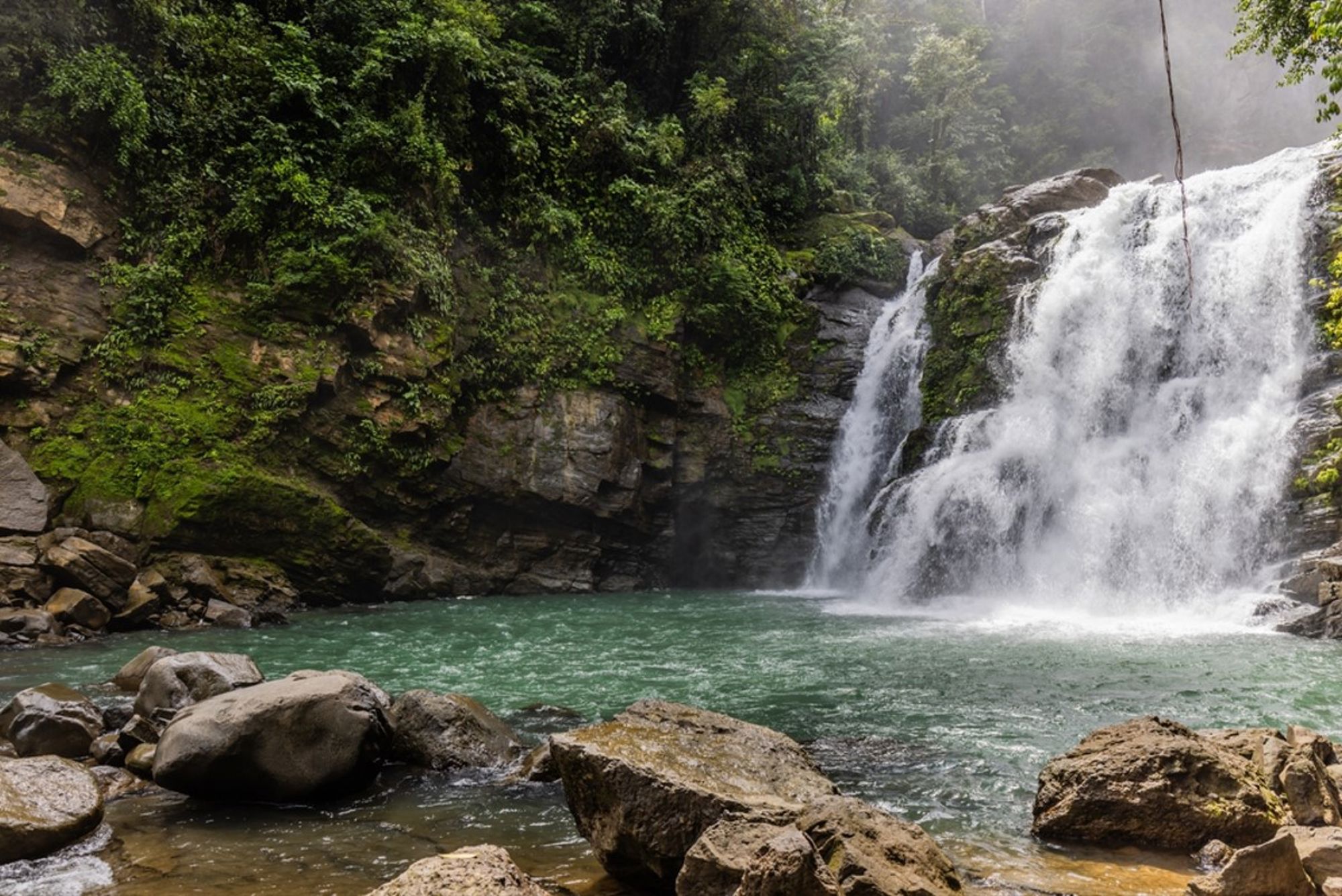 Waterval in het Costa Ricaanse regenwoud met turquoise lagune en rotsen op de voorgrond.
