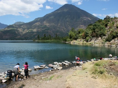 Meer Atitlán met vulkaan op de achtergrond in Guatemala, langs de oever wassen mensen kleding.
