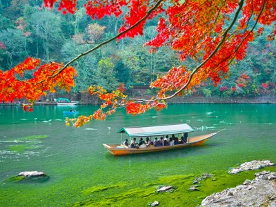 Boottocht over de Hozu-rivier bij Arashiyama, Kyoto, met rode herfstbladeren langs de oever.
