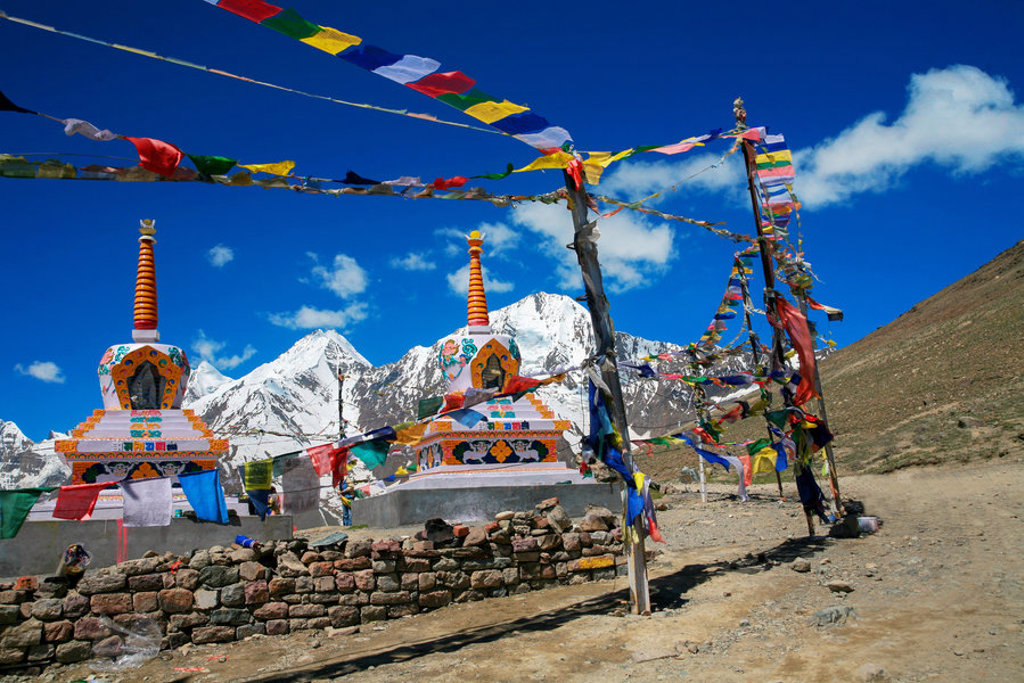 Boeddhistische stupa’s met gebedsvlaggen in Ladakh, met besneeuwde bergen op de achtergrond.
