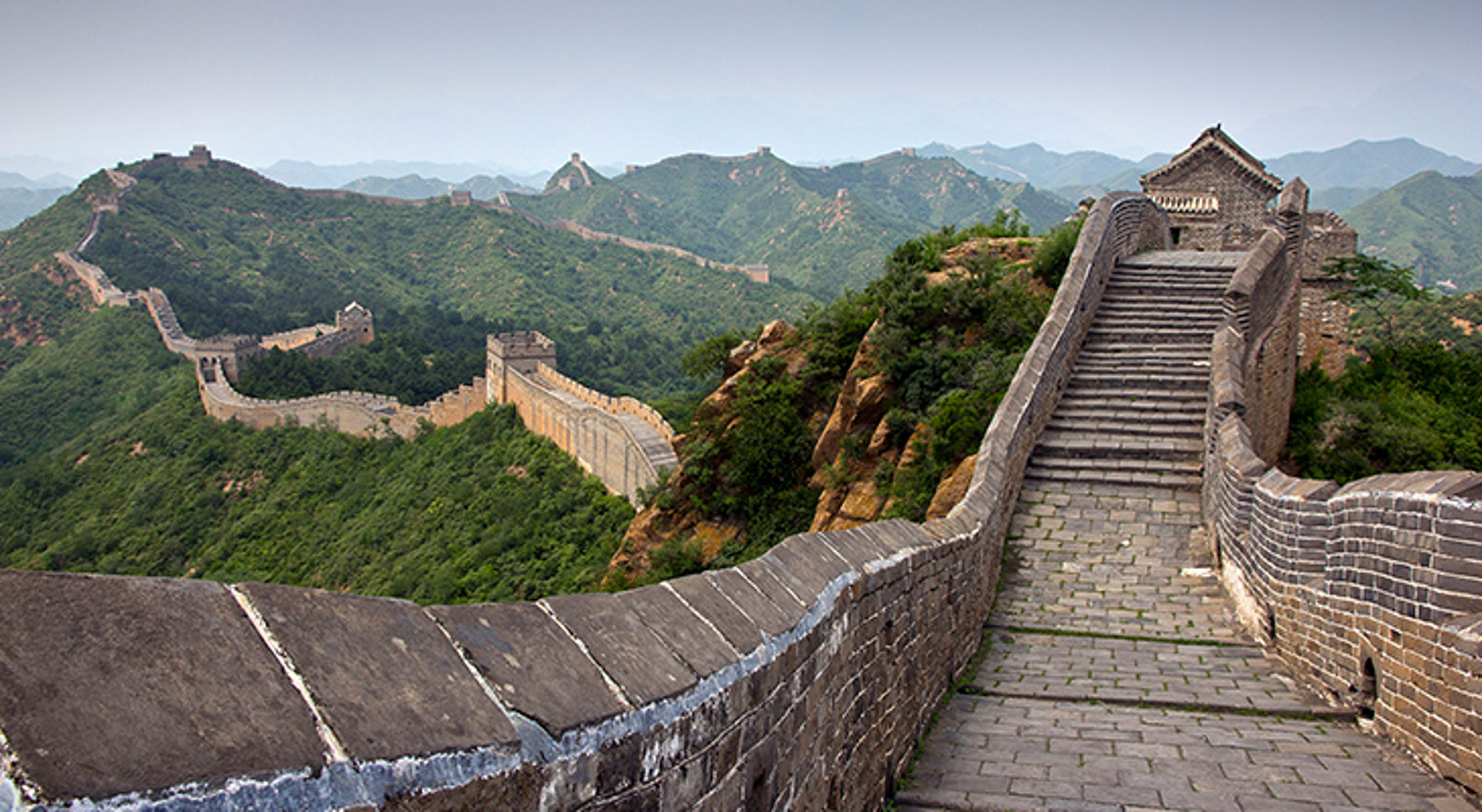 De Chinese Muur slingert over groene heuvels met wachttorens en een stenen trap naar een uitkijkpunt.