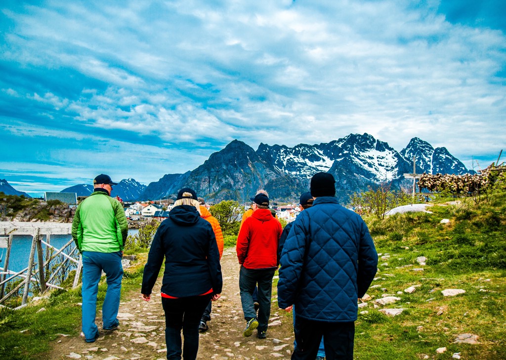 Groep wandelaars tijdens groepsrondreis Noorwegen met uitzicht op besneeuwde bergen en kustdorp.