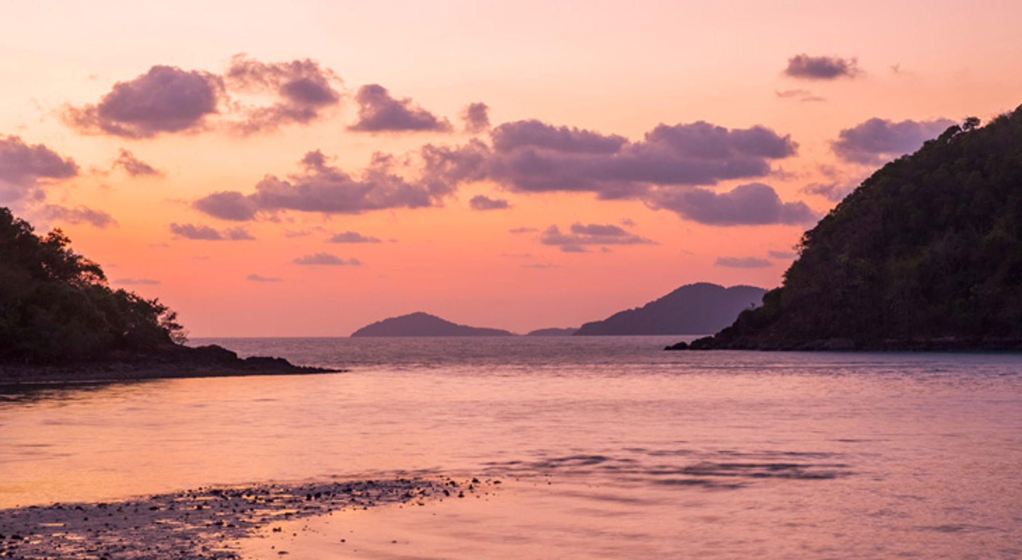 Zonsondergang boven de zee met silhouetten van eilanden en heuvels in Thailand.