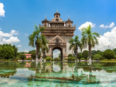 Patuxai-monument in Vientiane, Laos, met palmbomen en weerspiegeling in een vijver.
