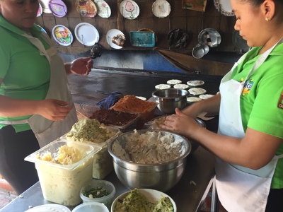 Twee koks bereiden pupusa’s met verschillende vullingen op een bakplaat in El Salvador.