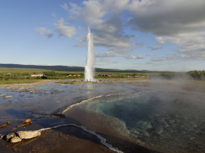 Geyser die hoog de lucht in spuit bij Geysir, met warmwaterbron op de voorgrond, Route IJsland.