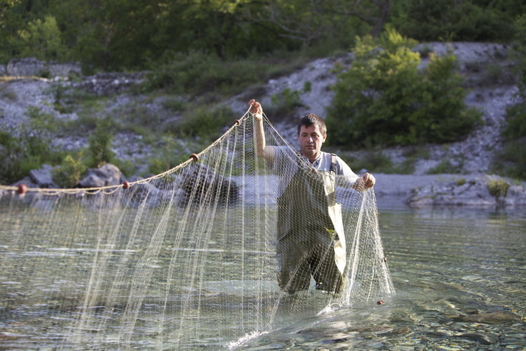 Visser haalt een visnet binnen in een heldere rivier in de Balkan.