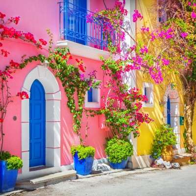 Kleurrijke Griekse straat met roze en gele huizen, blauwe deuren en bougainvillea in bloei tijdens 22-35ers reis Griekenland.