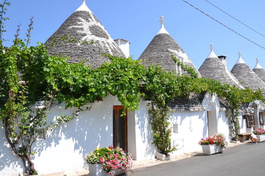Trulli-huizen met kegelvormige daken in Alberobello, Puglia, langs een straat met bloemen en wijnranken.