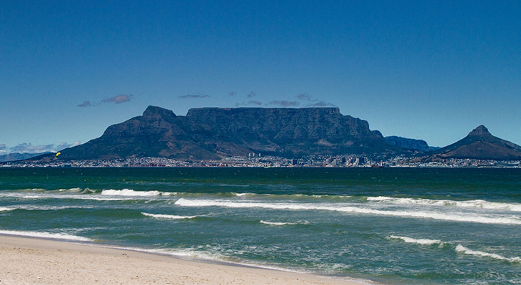 Uitzicht op de zee, Kaapstad en Tafelberg Tafelberg bij Kaapstad gezien vanaf het strand, met golven in de Atlantische Oceaan op de voorgrond.