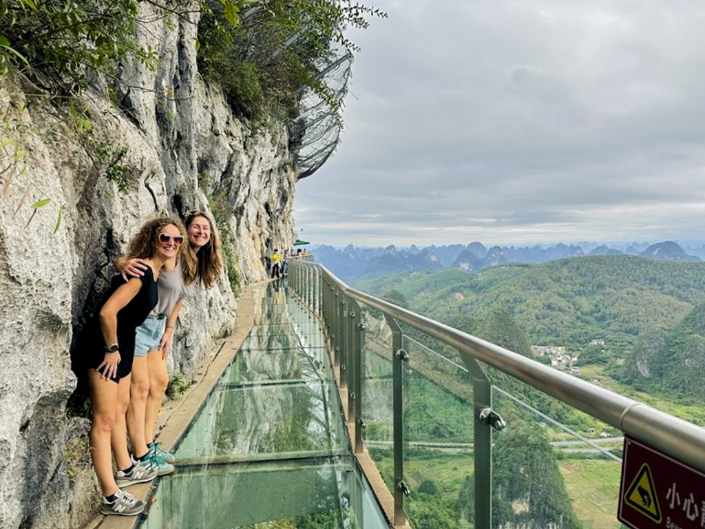 Gezin op glazen skywalk langs een rotswand met uitzicht op groene karstbergen tijdens familiereis China.