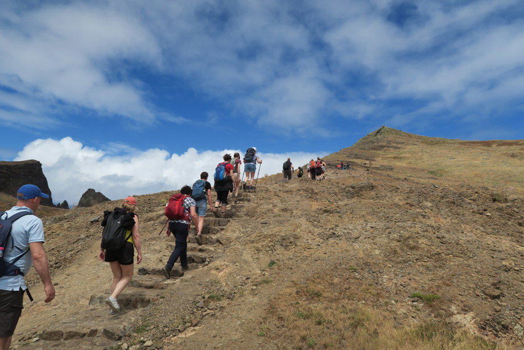 Wandelaars op bergpad tijdens wandelvakantie op Madeira, met uitzicht op ruig landschap en blauwe lucht.