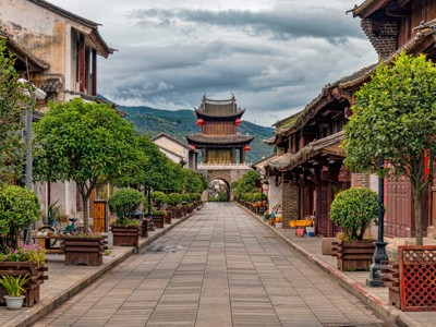 Straat in een oude Chinese stad met traditionele huizen en een poortgebouw in de verte.