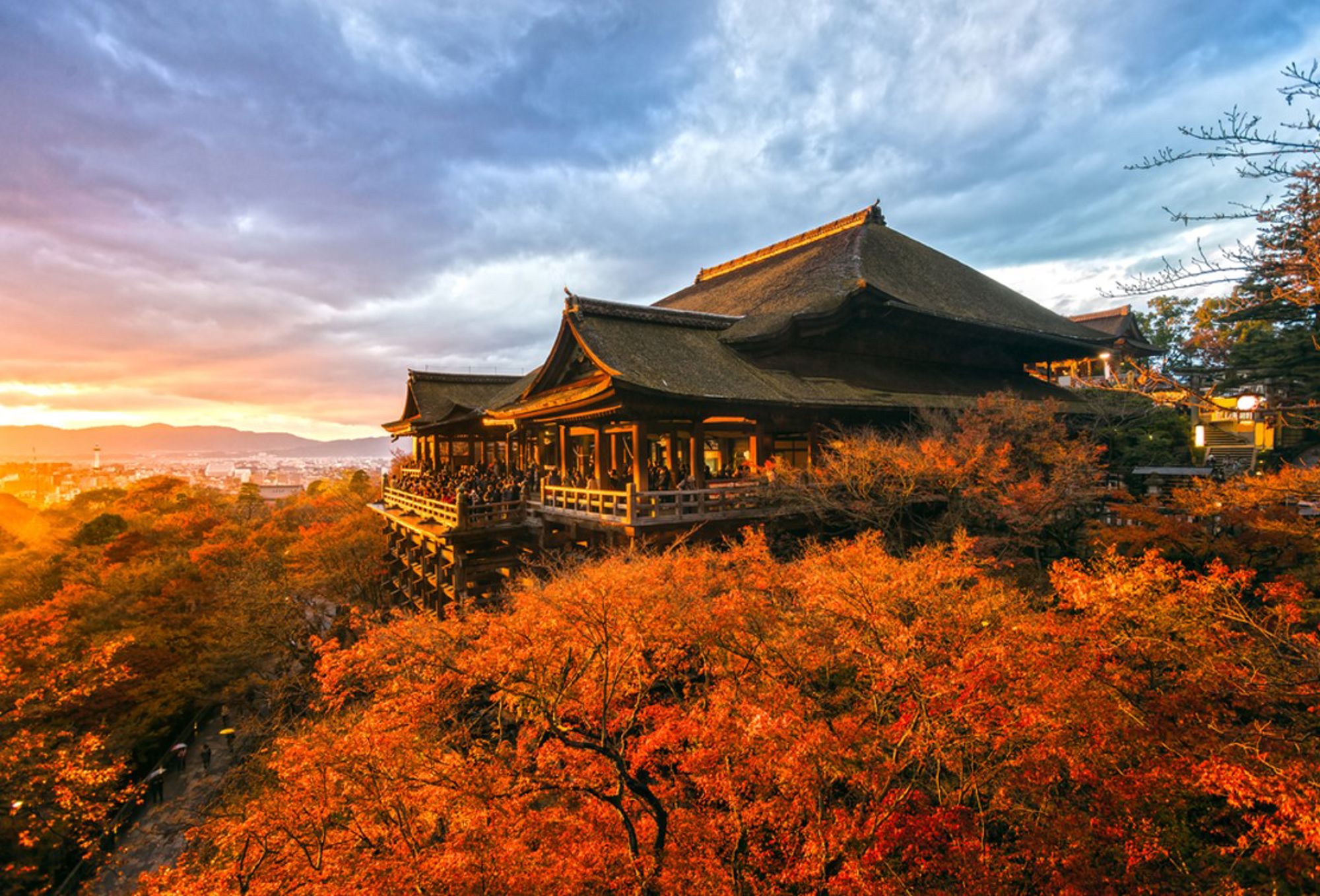 Kiyomizu-dera tempel in Kyoto bij zonsondergang, omringd door rode herfstbladeren.