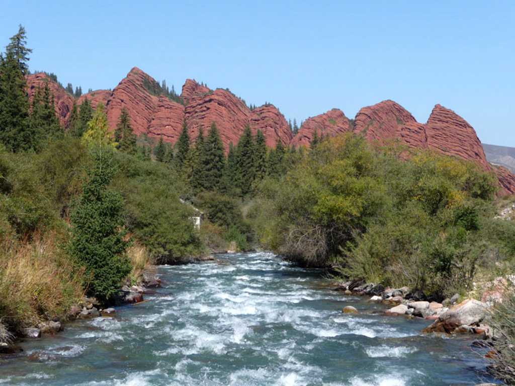 Rivier in een groene vallei met rode rotsformaties in Kirgistan, tijdens een wandelreis langs de Zijderoute.
