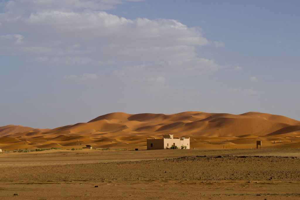 Woestijnduinen in Marokko met een klein huisje aan de rand van de Sahara.